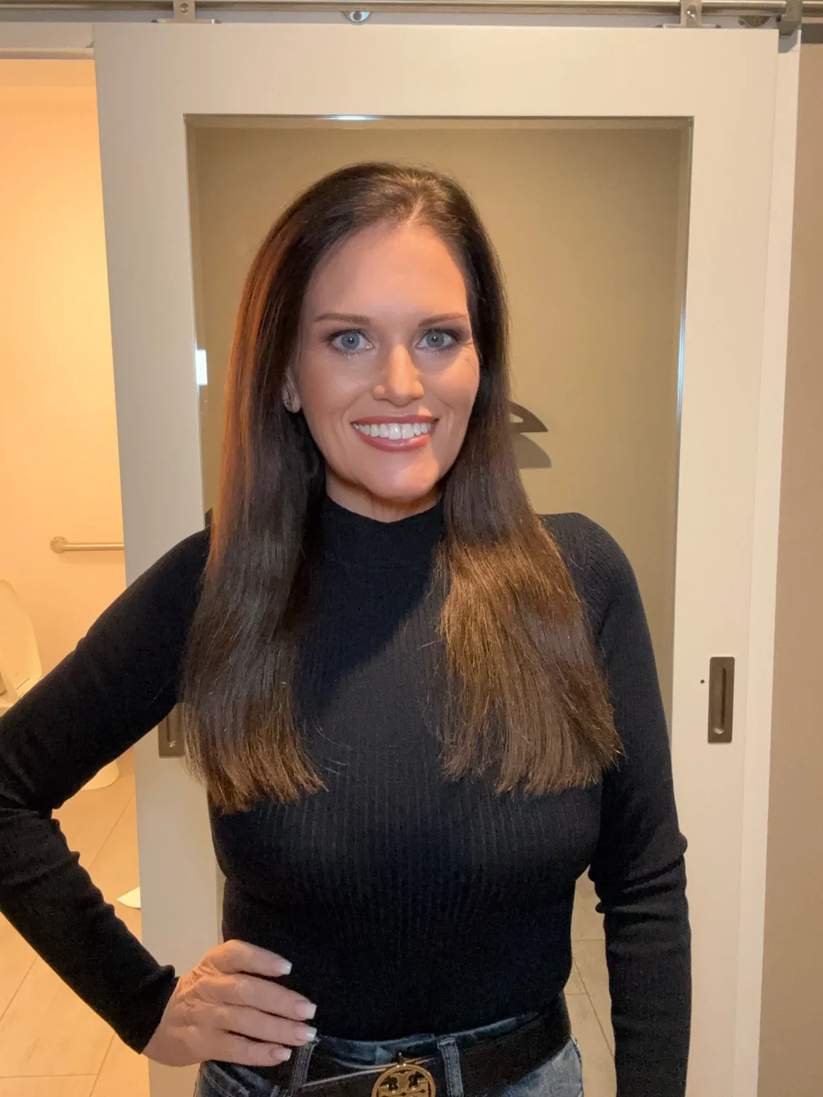 Rachel wearing a black mock neck top with dark high-rise denim and a gold-buckle belt.
